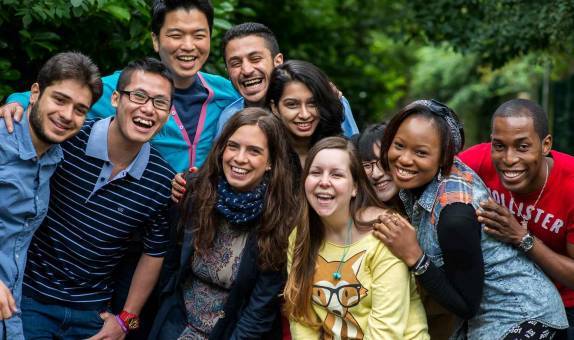 10 international students smiling and gathered closely together for a group photo in a green area. 