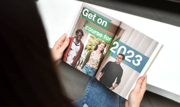 A postgraduate prospectus open on a page with the text 'Get on course for 2023'.